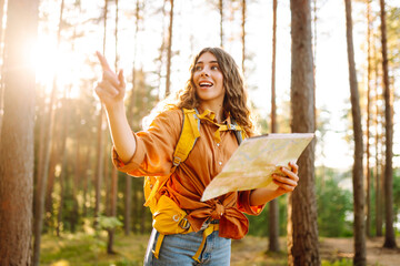 Naklejka premium Young woman holding map standing in forest. Relaxed woman hiker looking navigation searching route. Hiking concept