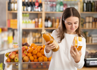European teenage girl took various varieties of juices from shelf, chooses fruit drink for dinner with friends. Client buys drinks and snacks for buffet