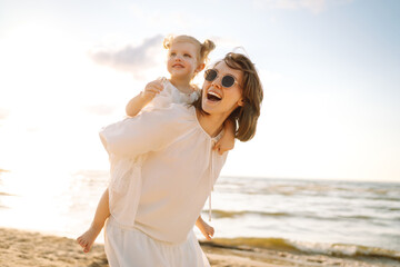 Smiling young mother and beautiful daughter having fun at the beach on the sunset. Childhood, fun, relaxation concept