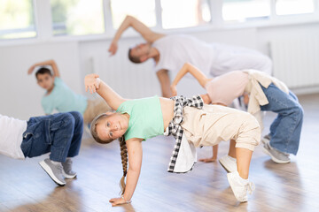 Young girl and group of children in casual wear training hip hop movements on floor in modern dance class with male coach