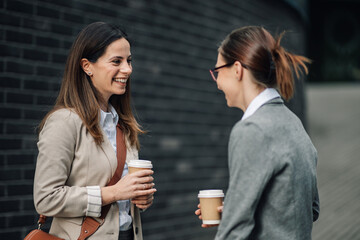 Two businesswomen chatting and smiling during coffee break outdoors