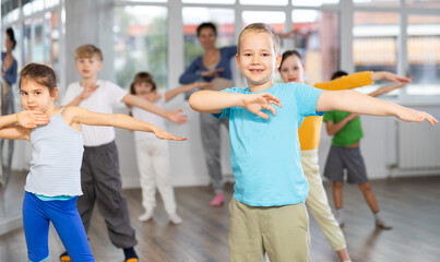 Dynamic little boy training hip hop dance poses with instructor and other attendees of dancing courses