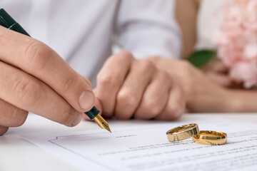 Newlyweds signing marriage contract and wedding rings on desk, selective focus