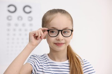Fototapeta premium Little girl wearing glasses near vision test chart at ophthalmologist office