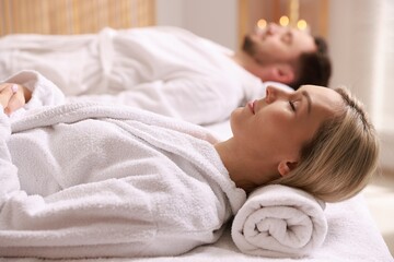 Couple in bathrobes lying on massage tables in spa salon, selective focus