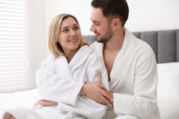 Fototapeta premium Spa. Happy couple in bathrobes sitting on bed indoors