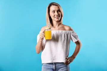 Woman with mason jar of orange juice on light blue background. Refreshing drink