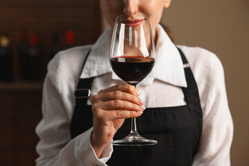 Professional sommelier tasting red wine in glass indoors, closeup