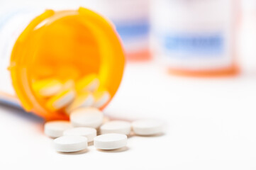 Round white prescription medication medicine pill tablets spilling from a bottle with numerous full bottles in background