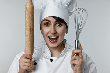 Excited chef with rolling pin and whisk on light grey background
