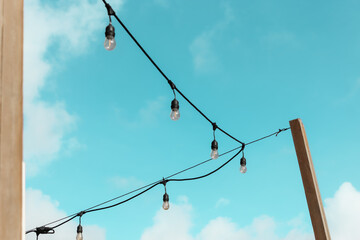 antique style string light bulbs hanging from a wood post outside isolated against the sky.  edge...