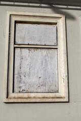 old window on an old building wall facade shuttered and boarded up with white plywood, likely for security or protection. architectural detail. blank with space for copy.
