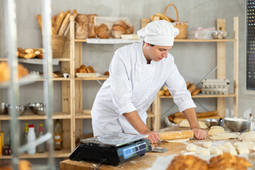 Making yeast dough in bakery - young male baker rolling out dough with a rolling pin