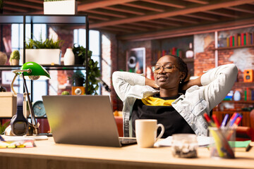Joyous woman laying down on desk chair, relaxing at home, watching TV show on laptop. Smiling person sitting back and enjoying leisure time in apartment, consuming entertainment media content