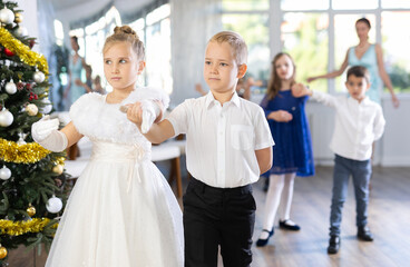 Couple of smiling tweens, boy and girl in festive clothing performing graceful waltz with group...