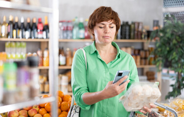Woman using phone and an online application scans the qr code on a package with champignons. Customer holds her phone and scans the barcode for payment at the store's checkout.