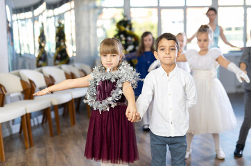 Pleased schoolboys and schoolgirls of primary classes standing in row performing dance position in events salon