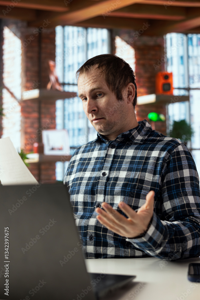 Aufkleber man at home office desk crosschecking information between laptop screen and paper files, seeing inac