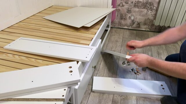 The man lays out wooden panels for assembling pull-out shelves. Linen shelves for the sofa bed