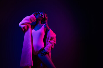 Attractive young woman in pink bodysuit and coat with neon lights, exudes glamour and luxury