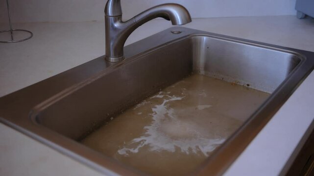 The stainless steel sink filled with murky, brown water, a drainage issue, clogged pipes, or contaminated water supply. Dirty water is coming back to the sink.