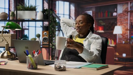 Woman watching movies at home on laptop, drinking coffee, paying close attention to screen. Cheerful person relaxing in apartment, enjoying film and hot beverage, camera B