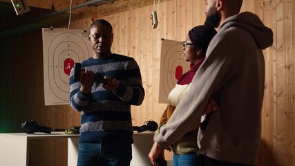 Shooting gallery safety officer demonstrating how to safely reload pistol and cock gun to clients,...