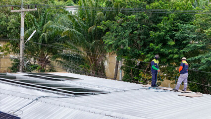 A sustainable energy project featuring solar panels on a roof surrounded by tropical trees,...