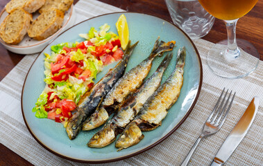 Appetizing fried sardines with a light vegetable salad made from lettuce, tomatoes and red pepper. Decorated with a slice ..of lemon