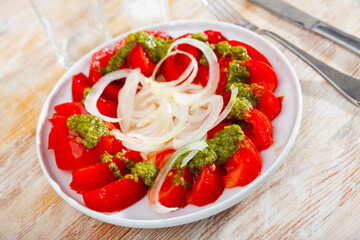 Sliced fresh tomatoes served with basil pesto sauce and onion. Italian style appetizer