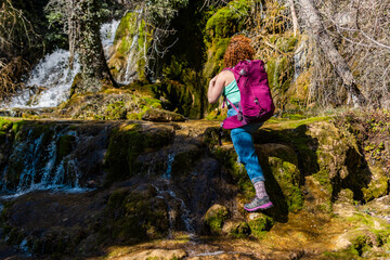 Female hiker crossing waterfall in lush green forest