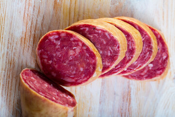 Thin salchichon sausage slices on wooden background, view from above