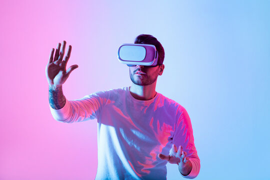 A person explores a virtual reality experience, wearing a headset while interacting with their surroundings. The vibrant pink and blue lights create an immersive atmosphere.