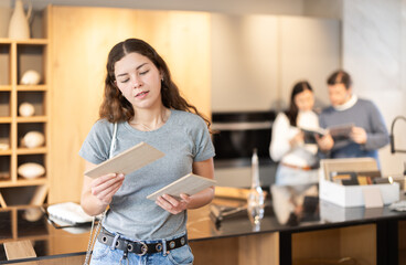 Female buyer with samples of material chooses kitchen set in a furniture store