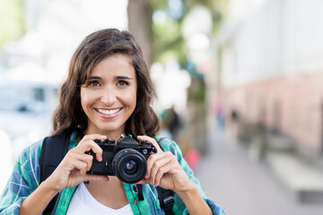 Smiling woman holding camera on city street, enjoying urban photography adventure, copy space