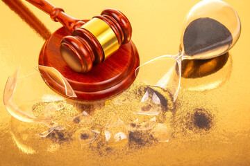 Close-up of a polished gavel next to a broken hourglass with dark sand, on a golden surface,...