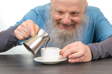 warm morning ritual: cheerful elderly man with long beard pours coffee into white cup on rustic wooden table, homemade breakfast ambiance