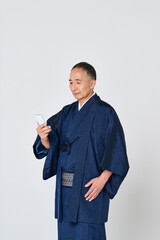 スマートフォンを使う紺色の着物を着たシニア男性