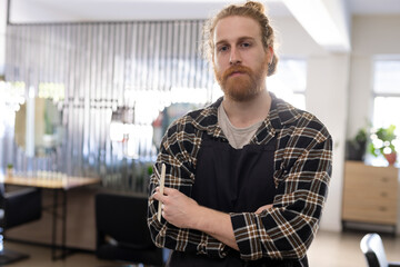 Barber with apron holding scissors in modern salon, looking confidently at camera, copy space