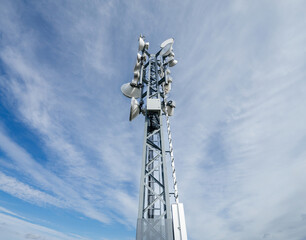 A towering communications tower stands against a backdrop of wispy clouds, equipped with LTE, 6G, and WiFi wideband technology.