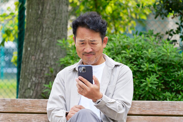 悩まみながら屋外でスマートフォンを見る中年の男性　屋外