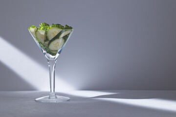 Cucumber slices in a martini on a neutral background with a beam of light.