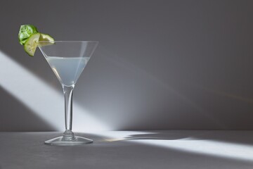 Cucumber martini with cucumber and mint on the rim, on a grey background with a beam of light.