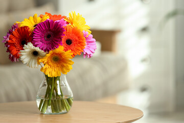 Bouquet of beautiful gerbera flowers in glass vase on wooden table indoors, space for text