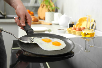 Man taking fried eggs from frying pan in kitchen, closeup