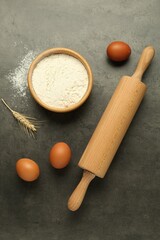 Rolling pin, bowl of flour, eggs and spike on grey table, flat lay