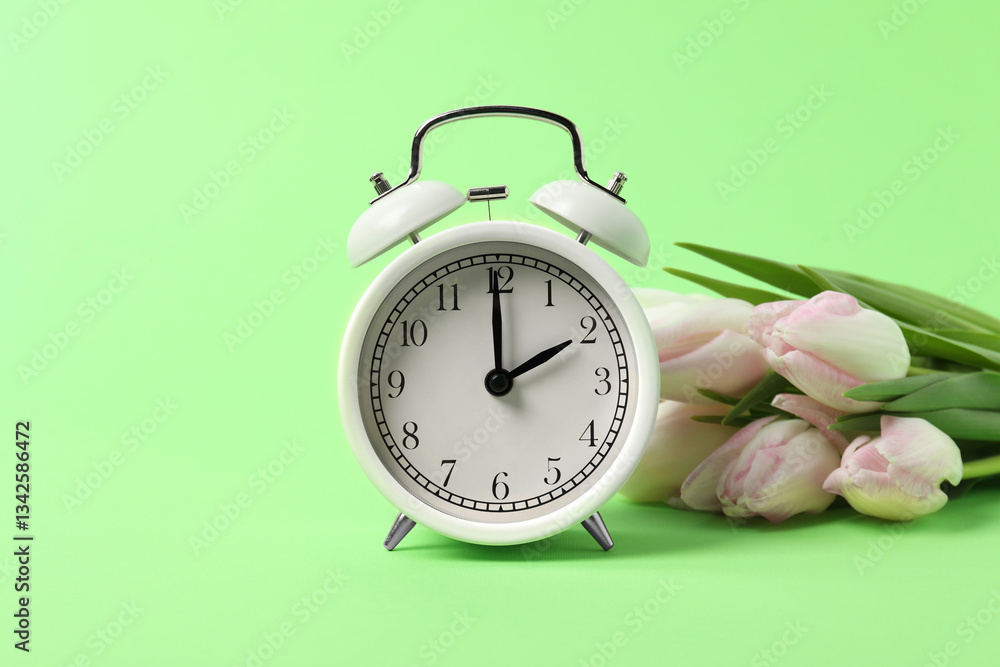 Poster spring time. alarm clock and beautiful tulips on green background