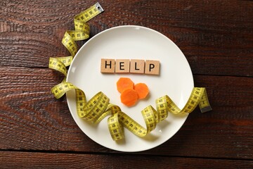 Bulimia. Squares with word Help, plate, cut carrot and measuring tape on wooden table, top view