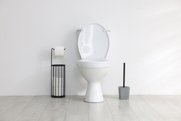 Toilet, brush and necessities near white wall