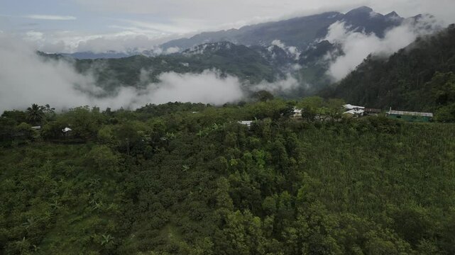 Drone flies over mountain ridge toward foggy valley with rolling clouds